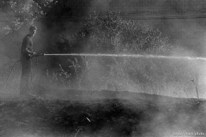 Firefighter with hose spraying Grassfire along the train tracks.