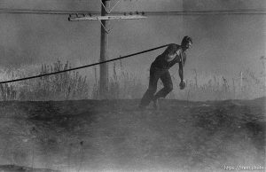 Firefighter pulling hose toward Grassfire along the train tracks.