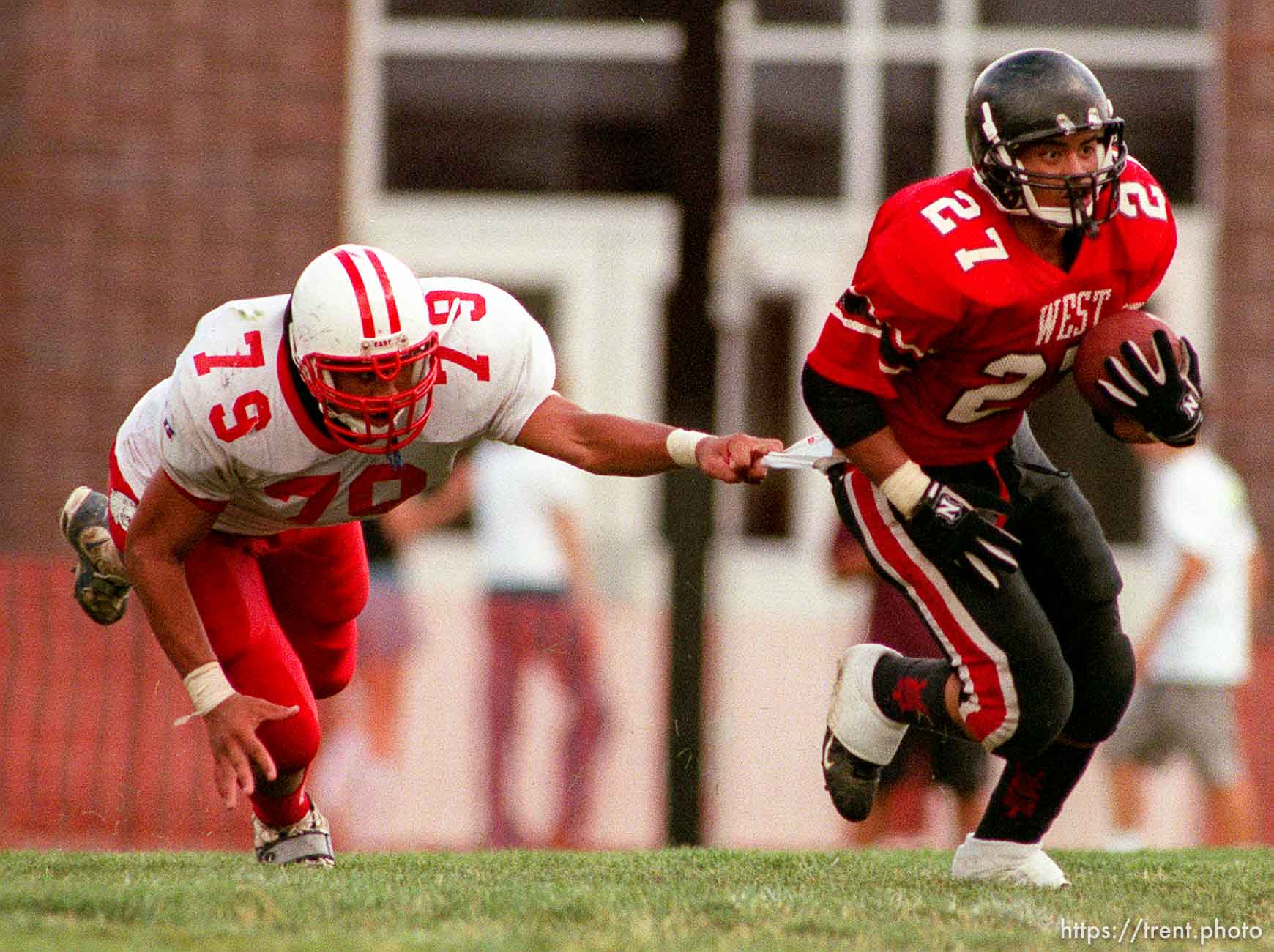 East's Ed Tuiono (#79, left) hangs onto West's Chris Alo's (#27, right) jersey at East vs. West football.
