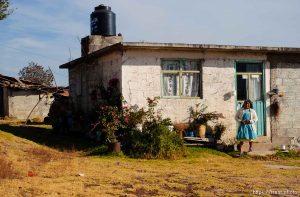 Socorro Avila Morales outside of her newer home (at rear left is the home she used to live in. Morales's children working in Utah have helped her afford to build a newer home than she previously lived in; 12.03.2004