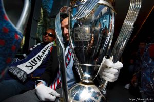 Real Salt Lake team equipment manager Kevin Harter wears white gloves holding the MLS Cup trophy on the team bus Tuesday, November 24 2009. Midfielder Andy Williams at left.