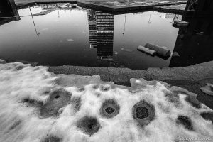 Shelled high-rise buildings reflected in pond.